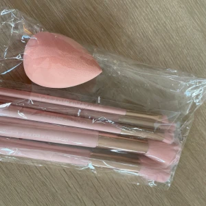 Rosa sminkborstar & beautyblender set - Säljer ett set med flera sminkborstar och en rosa beautyblender från Makeup Mekka. Borstarna har ljusrosa skaft och guldiga detaljer, perfekta för att applicera smink med precision. Beautyblendern är mjuk och droppformad för enkel applicering av foundation.