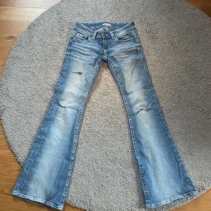 Bootcut lågmidjade jeans Gina Young  - Bootcut jeans från Gina Young i storlek xs i ljusblå tvätt med slitningar på framsidan och snygga detaljerade bakfickor med knappar, tre hål på framsidan. Lågmidjade och tillverkade i klassiskt jeanstyg. Perfekt för dig som gillar lågmidjat. Använda tre-fem gånger.