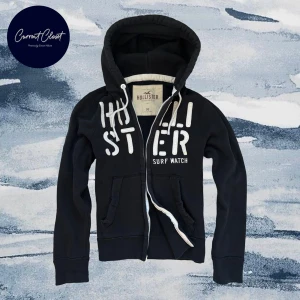 Svart hoodie från Hollister med tryck - Svart hoodie från Hollister med vit broderad logga och texten 'Surf Watch' på bröstet | Bredd: 40cm Längd: 63cm | Size M | 