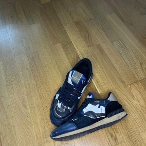 Valentino Garavani camo sneakers - Snygga sneakers från Valentino Garavani med blå, svarta och grå camouflage-detaljer. Skorna har svarta snören, rund tå och coola kontraster i material som mocka och textil. Perfekta för dig som vill sticka ut med exklusiva och trendiga sneakers. Använda rockrunner dem är äkta dock har jag ut boxen till dem men pris kan diskuteras fraktar samma dag! 