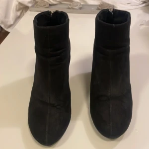 Svarta mocka stövletter med klack - Snygga svarta stövletter i mocka med spetsig tå och kraftig klack. Skorna har dragkedja bak i silverfärg som detalj och en stilren, enkel design. Perfekta för dig som gillar en klassisk men trendig look. Storlek 40, men passar även dig med storlek 39