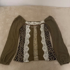 off shoulder topp  - Säljer en unik brun offshoulder topp från Shine&She med långa ärmar. Framsidan har leopardmönster, vita spetsdetaljer och snörning i mitten. Toppen har en figurnära passform och coola vintagevibbar. Perfekt för dig som vill sticka ut!