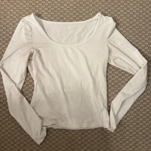 Vit långärmad topp med rund hals - Säljer en enkel och stilren vit långärmad topp med rundad halsringning. Toppen är gjord i mjukt bomullsmaterial och har en normal passform som sitter snyggt på kroppen. Perfekt att matcha med jeans eller kjol för en clean look.
