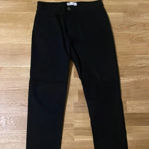 Svarta slim fit byxor från Denim Co - Svarta byxor från Denim Co i slim fit-modell. Klassisk femficksdesign med bälteshällor och knappstängning. Snygg och enkel stil som passar till det mesta. Materialet är mjukt och stretchigt för extra komfort.