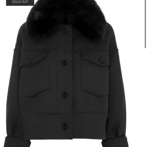 Svart Charlie jacka från Meotine - Säljer en svart Charlie jacka från Meotine med stor, fluffig fuskpälskrage. Jackan är croppad, har två stora bröstfickor med lock och knappar framtill. Stilren och boxig passform, perfekt för dig som gillar statement-kragar och minimalistisk look.