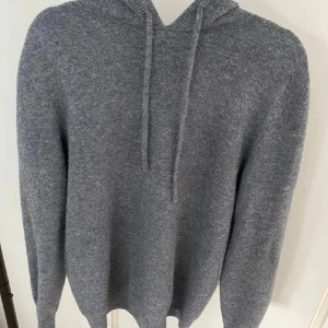 John henric Kashmir hoodie  - Mysig grå kashmir hoodie från John henric med huva och dragsnören. Tröjan har lång ärm och en avslappnad passform, perfekt för kyliga dagar. Enkel och stilren design som funkar till det mesta. Materialet är mjukt och skönt mot huden.