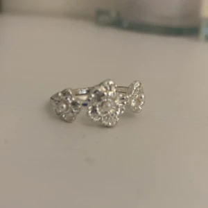 Smyckeset med silverringar och pärlarmband - Set med två silvriga ringar och ett armband med ljusrosa pärlor. Ena ringen har tre små blommor i silver, den andra har en öppen hjärtformad design. Armbandet består av oregelbundna pärlor och ett mörkt hjärthänge. Perfekt för dig som gillar söta och romantiska detaljer. Ej riktigt silver!