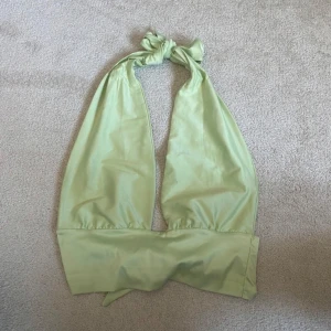 Ljusgrön topp Gina Tricot - Snygg ljusgrön topp från Gina Tricot med knyt både i nacken och baktill. Toppen har en halterneck-design och är tillverkad i ett mjukt, glansigt material som ger en fräsch look. Perfekt för att skapa en trendig och chill outfit.