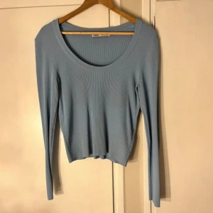 Ljusblå ribbad topp från Zara - Säljer en ljusblå långärmad topp från Zara med ribbad struktur och rundad halsringning. Modellen är croppad och har en slim passform som sitter snyggt på kroppen. Perfekt att styla med jeans eller kjol för en fräsch look.