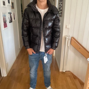 Svart Moncler pufferjacka med huva - ( Pris kan diskuteras )Säljer en svart glansig pufferjacka från Moncler med huva och dragkedja. Jackan har Moncler-logga på ärmen, flera fickor och en riktigt fet, vadderad look. Perfekt för dig som vill ha en stilren och varm jacka med streetkänsla.