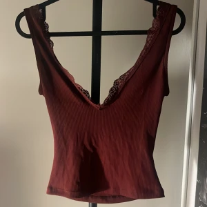 Vinröd ribbad linnetopp från NA-KD - Säljer en vinröd ribbad linnetopp från NA-KD i storlek XS. Toppen har v-ringad hals med spetskant och är ärmlös. Materialet är mjukt och stretchigt, perfekt för att skapa en snygg och chill look. Passformen är slim och toppen är croppad. Har andvänt 3-4 gånger:)