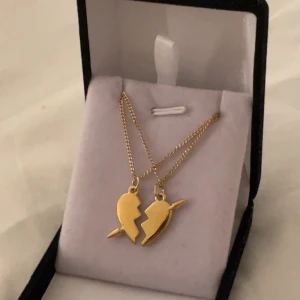 Guldiga halsband med hjärthänge - Två guldiga halsband med matchande hängen i form av ett delat hjärta, där varje del har en pil genom sig. Perfekt som vänskapshalsband eller för att dela med någon speciell. Kedjorna är tunna och eleganta, och hjärthängena har en cool, kantig design.
