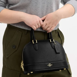 Svart handväska från Coach i skinn - Snygg svart handväska från Coach i äkta skinn med rundad form och guldfärgade metalldetaljer. Väskan har två handtag, avtagbar axelrem och dragkedja upptill. Coach-logga i guld framtill och en klassisk tag. Perfekt storlek för det viktigaste. Köptes i London för 2 års sedan, nu är den slutsåld och väldigt svår att få tag på. Köptes för 3600 säljer för 3000 då den är knappt använd. Obs Kartong etc inkluderar inte.