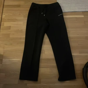 Svarta mjukisbyxor från Les Deux - Mörkblåa byxor från Les Deux med diskret logga på vänster höft. Byxorna har dragsko i midjan och raka ben. Sköna och stilrena, perfekta för chill eller streetwear. Materialet känns mjukt och stretchigt.