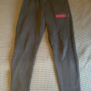 Svarta mjukisbyxor från Hoodrich - Svarta mjukisbyxor från Hoodrich med röd logga på benet och snörning i midjan. Byxorna har en bra passform och är tillverkade i mjukt bomullsmaterial. Perfekta för en chill och avslappnad stil.
