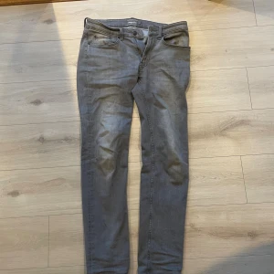 Grå jeansbyxor från Dressmann Regular Fit - Snygga grå jeansbyxor från Dressmann i modellen Regular Fit. Klassisk femficksdesign, raka ben och normal passform. Byxorna är tillverkade i ett mjukt bomullsmaterial med dragkedja och knapp framtill. Perfekta för en stilren och avslappnad look.