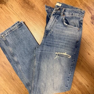 Blå ripped jeans från Gina Tricot - Snygga blåa jeans med slitna detaljer och hål vid knäna och låret. Modellen har hög midja och raka ben. 