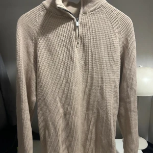 Beige stickad half zip - Säljer en beige stickad tröja med ribbad struktur och hög krage med half zip-dragkedja. Tröjan har långärmad passform och är perfekt för lager-på-lager under kyliga dagar. Enkel och stilren design som funkar till det mesta. Bra pass form o lätt att styla.