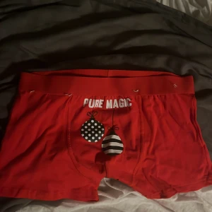 Röda julboxers med print, strl S - Röda boxershorts med texten 'PURE MAGIC' framtill och 'CHECK OUT MY BALLS' baktill. Framtill finns två julgranskulor i svartvitt mönster. Perfekta för julen och med stretchig resår i midjan. Materialet är mjukt och skönt, troligen bomull och polyester.