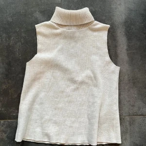 Beige stickad polo - Snygg beige stickad polotopp. Modellen är ärmlös och har en rak passform som sitter bekvämt. Perfekt att styla med jeans eller kjol för en clean look eller till något finare tillfälle. Säljer då den inte kommer till användning längre💕