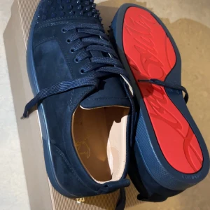 Christian Louboutin sneakers mörkblå, nya, stl 43 - Säljer ett par Christian Louboutin sneakers i storlek 43. Skorna är helt nya och aldrig använda, levereras med originalkartong, dustbag och tillbehör. Färg: Mörkblå med den klassiska röda sulan elegant och lyxig design som passar perfekt till både vardag och fest.  Äkta vara, köpta i butik. Perfekta för dig som vill ha ett par exklusiva sneakers i toppskick till ett riktigt bra pris!
