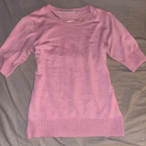 Ljusrosa stickad tröja från Kappahl - Supersöt ljusrosa stickad tröja från Kappahl med rund halsringning och halvlånga ärmar. Tröjan har ribbade muddar vid ärmslut och nederkant, vilket ger en snygg och enkel look. Perfekt för dig som gillar en feminin och stilren vibe.