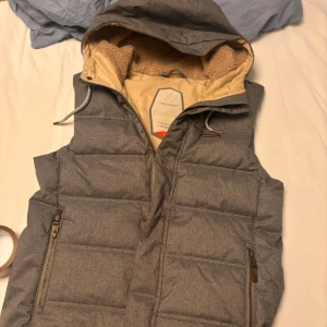 VÄST MED LUVA  - Säljer du denna as feta västen med luva och fodrad i luvan! Rejäl väst i sin fina gråa färg storlek S passar M 