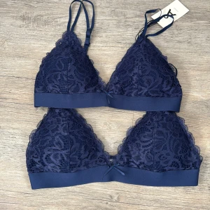 Mörkblå spets bh från Åhlens  - Bara att skriva om ni inte vill ha båda, en för 75, båda för 150kr!                      Två mörkblå braletter från Å Woman i storlek M. De har v-ringad form, justerbara axelband och är tillverkade i mjuk spets med små rosetter framtill. Bred resår under bysten för extra komfort och hakknäppning bak. Perfekt för en snygg och bekväm look.