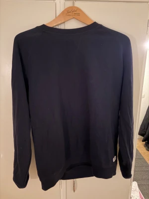 Mörkblå långärmad sweatshirt - En enkel och stilren mörkblå sweatshirt med rund hals och lång ärm. Tröjan har en normal passform och är tillverkad i mjuk bomull, perfekt för chill dagar. Diskret liten etikett nertill på sidan. Passar dig som gillar basic och cleana plagg.