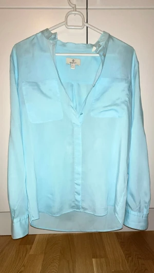 Gant - Ljusblå skjorta från Gant, strl 36 / bra skick!  - Snygg ljusblå skjorta från Gant i storlek 36. Skjortan har lång ärm, två bröstfickor och klassisk krage utan knappar. Tillverkad i ett mjukt och svalt material som ger en skön känsla. Perfekt för dig som gillar stilrena och enkla plagg.