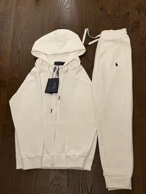 Vita mjukisbyxor från Polo Ralph Lauren - Säljer ett par fräscha vita mjukisbyxor från Polo Ralph Lauren med klassisk logga broderad på benet. Byxorna har elastisk midja med snörning och är gjorda i mjukt bomullsmaterial för maximal komfort. Perfekta för chill dagar eller när du vill vara extra bekväm.