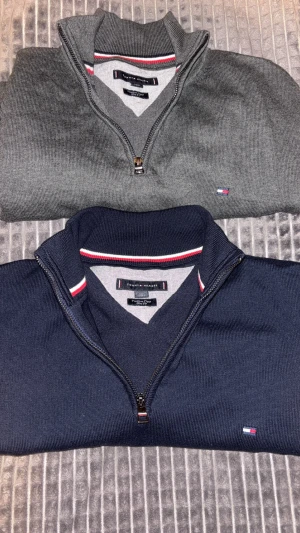 Marinblå och grå 1/4 zip tröjor från Tommy Hilfiger - Två snygga tröjor från Tommy Hilfiger i marinblått och grått. Perfekt för dig som gillar stilren look och vill uppgradera ditt game inom mode…😎👌Köper man båda kan vi lösa någon kampanj🤩