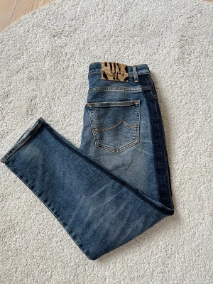 Jacob Cohën jeans - Snygga blå jeans från Jacob Cohën i klassisk tvätt med slitningar och coola detaljer. Modellen har raka ben, fem fickor och orange kontrastsömmar. Tillverkade i mjukt bomullsjeansmaterial, med exklusiv italiensk design och logotyp på bakfickan.
