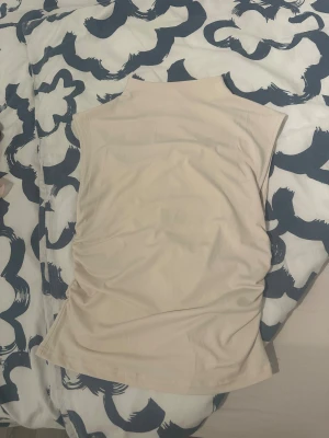 Beige polotopp i mjukt material - Säljer en stilren beige polotopp med ärmlös design. Toppen har en hög krage och är gjord i ett mjukt, stretchigt syntetmaterial som sitter skönt mot kroppen. Perfekt för dig som gillar minimalistisk och clean stil.