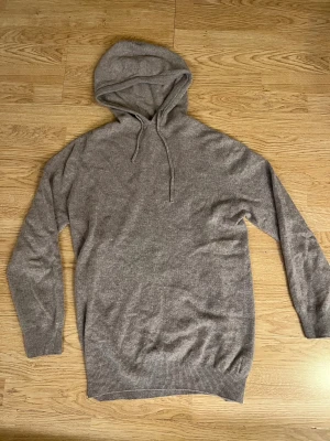 Garde Grisch Merinoull hoodie - Mjuk och lyxig beige hoodie från GardeGrisch i storlek M. Tröjan är stickad i merinoull och har huva med snörning samt ribbade muddar vid ärmslut och nederkant. Perfekt för dig som gillar chill och stilren look.