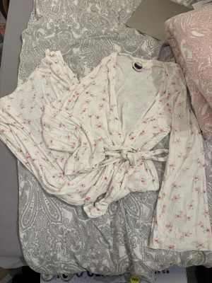 Blommig morgonrock från Gina Tricot - Supersöt vit morgonrock från Gina Tricot med små rosa blommor och långa ärmar. Morgonrocken har knyt i midjan och är gjord i mjuk bomull.