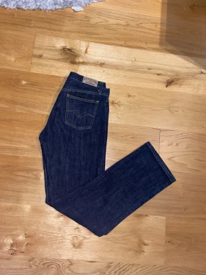 Replay jeans mörk blå (Regular fit) 29/30 - Snygga mörkblå jeans från Replay med klassisk rak passform och kontrastsömmar. Modellen har fem fickor och tydliga Replay-detaljer på bakfickorna. Tillverkade i 100% bomull för en skön känsla och stilren look.