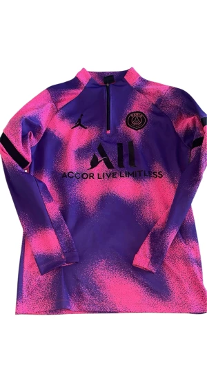 PSG x Jordan långärmad fotbollströja - Säljer en fet PSG x Jordan långärmad träningströja i syntetmaterial. Tröjan har en cool lila och rosa färg med spräckligt mönster, halv dragkedja och svarta loggor på bröstet. Perfekt för dig som vill sticka ut på planen eller träningen.
