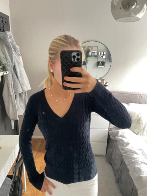 Mörkblå stickad tröja med v-ringning - Säljer en mörkblå stickad tröja med snygg v-ringning och kabelstickat mönster. Tröjan har lång ärm och sitter figurnära utan att vara för tight. Perfekt att matcha med kjol eller jeans för en clean look.