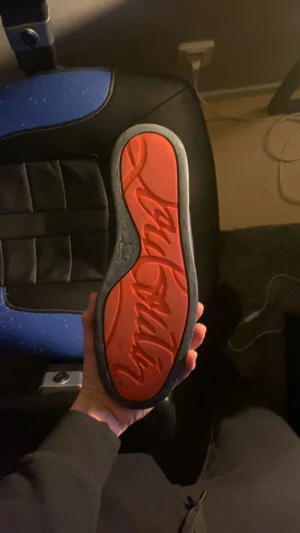 Loubssss - Säljer ett par snygga mörkblå sneakers från Christian Louboutin med den ikoniska röda sulan och signatur på undersidan. Skorna har snörning och är tillverkade i mocka med platt sula. Perfekt för dig som vill sticka ut med exklusiv stil.