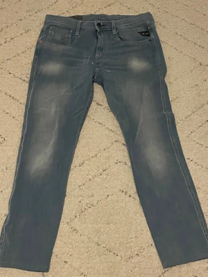 Replay Anbass ljusblå jeans, stl 31 - Snygga Replay Anbass jeans i ljusblå tvätt med diskreta slitningar och klassisk femficksdesign. Modellen har normal passform och raka ben, med Replay-logga på fickan och bak på linningen. Perfekta för dig som gillar stilrena och bekväma jeans.Pris går att diskutera!!