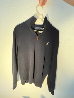 Mörkblå quater zip tröja Polo Ralph Lauren storlek S - Mörkblå långärmad tröja från Polo Ralph Lauren med klassisk broderad logga på bröstet. Tröjan har en snygg half zip-dragkedja med läderdetalj och hög krage. Perfekt för lager-på-lager och chill stil.
