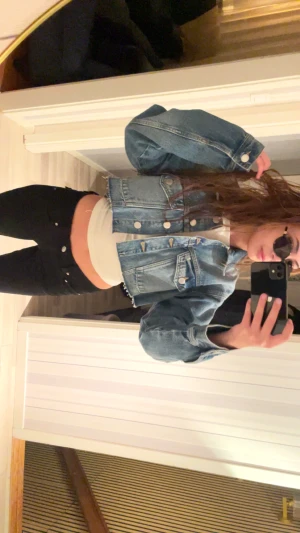 Croppad jeansjacka med silverknappar - Säljer en croppad blå jeansjacka med klassisk krage och stora silverfärgade knappar. Jackan har två bröstfickor med lock och rå kant nertill för en edgy vibe. Perfekt till ett par svarta jeans och sneakers.