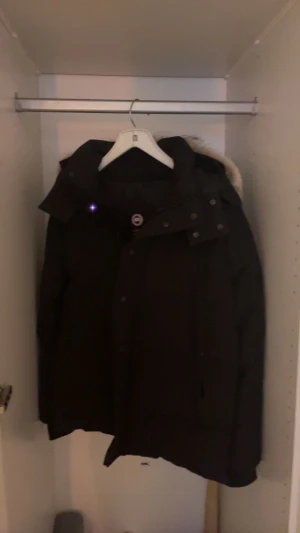 Svart Canada Goose dunjacka med päls - Säljer en svart dunjacka från Canada Goose med stor huva och beige pälsdetalj. Jackan har klassisk patch på ärmen, dragkedja och knappar framtill. Perfekt för kalla vinterdagar köpt i butik för 15000:- säljs för mer en halva pris finns i Norrköping tar emot byten också 