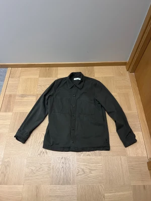 Mörkgrön overshirt från Samsøe Samsøe - Snygg mörkgrön overshirt från Samsøe Samsøe med klassisk krage och två stora bröstfickor. Tröjan är i stort sett i nyskick. Dvs 7/10. Använd ca 5 gånger. Säljer den på grund av att jag fick en likadan när jag fyllde år. Storleken är M
