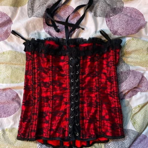 Röd och svart korsett - Snygg röd och svart korsett med spetsdetaljer och snörning framtill. Perfekt för att ge en edgy touch till din outfit. Den har en dragkedja på sidan för enkel på- och avtagning.