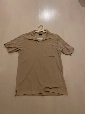 Beige frottéskjorta Firefly S - Beige skjorta från Firefly i mjuk frotté, perfekt för chill dagar. Klassisk krage, kort ärm och bröstficka ger en avslappnad vibe. Passformen är normal och materialet känns skönt mot huden. Enkel och stilren design utan mönster.