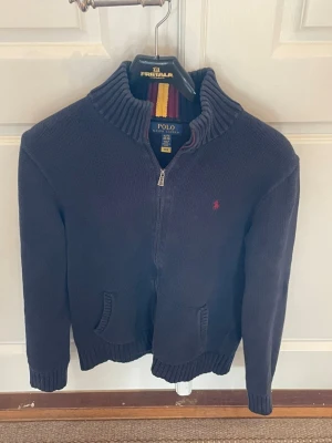 Mörkblå stickad kofta från Polo Ralph Lauren - Tjena! Säljer min snygga mörkblå stickade kofta från Polo Ralph Lauren med dragkedja framtill. Tröjan har två fickor och den klassiska röda Polo-loggan broderad på bröstet. Skick: 8/10. Storlek: Junior polo Ralph lauren XL 18-20 år men passar S/M 173-183. Bara att fråga om det är något. Priset går att diskutera!😊