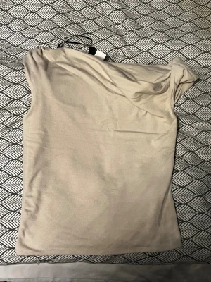 Beige ärmlös topp från DIVIDED - Snygg beige topp från DIVIDED i storlek XXS. Modellen är ärmlös med en enkel och clean design, perfekt för dig som gillar minimalistisk stil. Materialet känns mjukt och lätt mot huden, och färgen är neutral vilket gör den enkel att matcha med andra plagg.