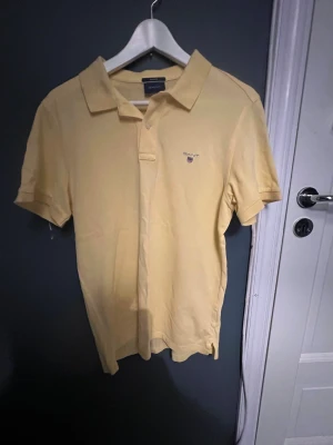 Gul pikétröja från GANT i bomull - Klassisk gul pikétröja från GANT i regular fit. Tröjan har korta ärmar, krage och knappar framtill. Broderad GANT-logga med sköld på bröstet. Perfekt för en avslappnad och stilren look.